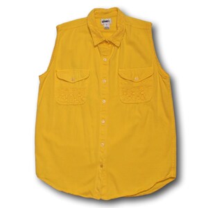 May include: A sleeveless, button-down shirt in a vibrant yellow hue. The shirt features two front pockets with delicate lace detailing and a collared neckline. The brand name "GRAND" is visible on the label.