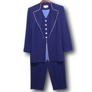May include: A navy blue suit set, comprising a long jacket with white trim and matching trousers. The jacket has a notched collar and decorative buttons. The suit is displayed on a wooden hanger.