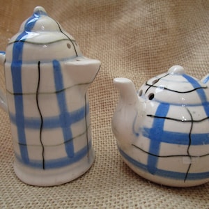 May include: A set of two ceramic salt and pepper shakers. The shakers are white with blue and black plaid patterns. The salt shaker is shaped like a teapot and the pepper shaker is shaped like a coffee pot.