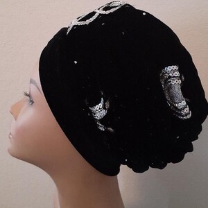Pode incluir: Um turbante de veludo preto com lantejoulas prateadas. O turbante é usado em uma cabeça de manequim.