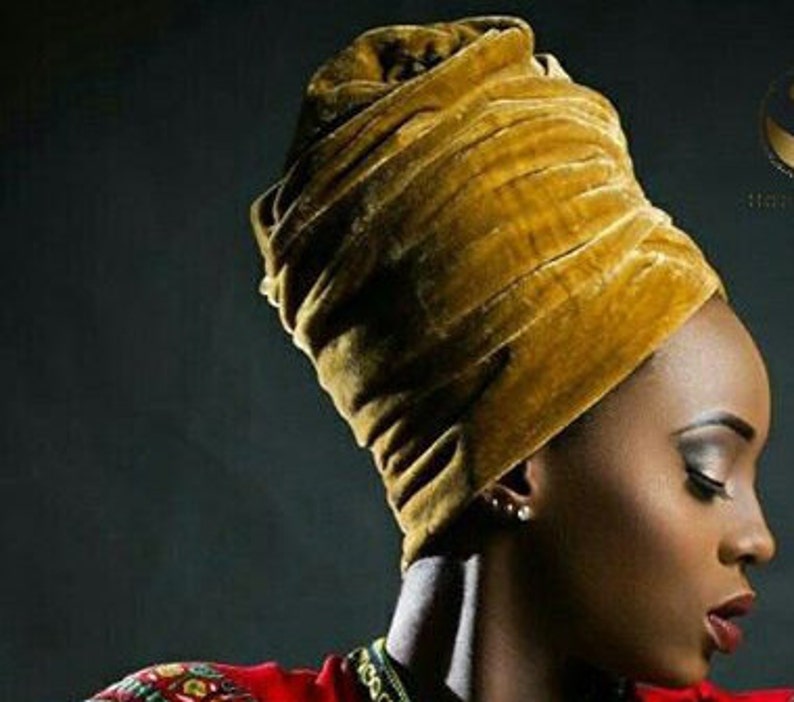 May include: A mustard yellow velvet turban headwrap. The turban is wrapped in a thick, luxurious fabric.