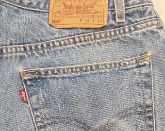 May include: Light blue denim jeans with a classic five-pocket design. The back pocket features a red Levi's tag. A brown leather patch at the waistband displays the Levi Strauss & Co. logo and size information: W34 L32.