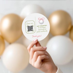 May include: A round white gift registry card with a QR code and the text "Scan me." The card also includes the text "Gift Registry" and "Thank you!" in pink. The background features gold and white balloons.