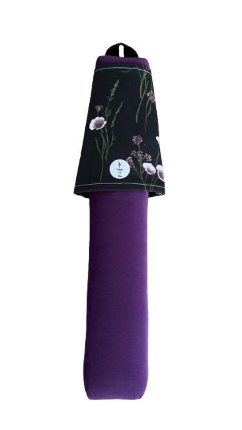 May include: A purple yoga mat carrier with a black floral patterned top. The top features white and purple flowers and green stems. A small white circular tag is visible on the top. The carrier has a black handle.