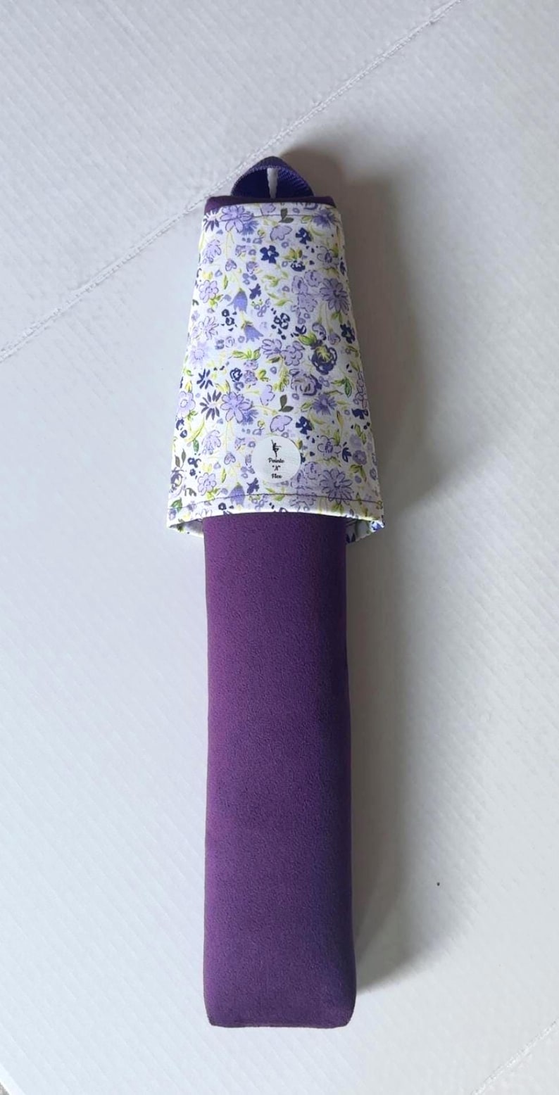 May include: A purple bolster pillow with a floral patterned cover. The cover is white with small purple and blue flowers. The pillow is approximately 12 inches long.