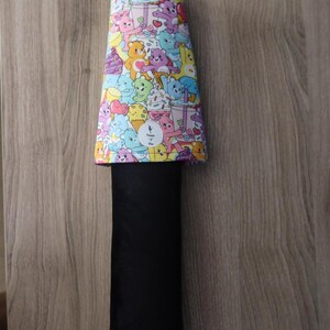 May include: A black and colorful Care Bears themed item. The top portion features a vibrant pattern of various Care Bears characters, ice cream, and other treats. The item has a black, rectangular body and a purple loop at the top.