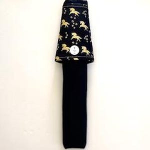 May include: A black necktie with a gold horse pattern on the top portion. The tie is folded and has a small, round white tag. The background is plain white.