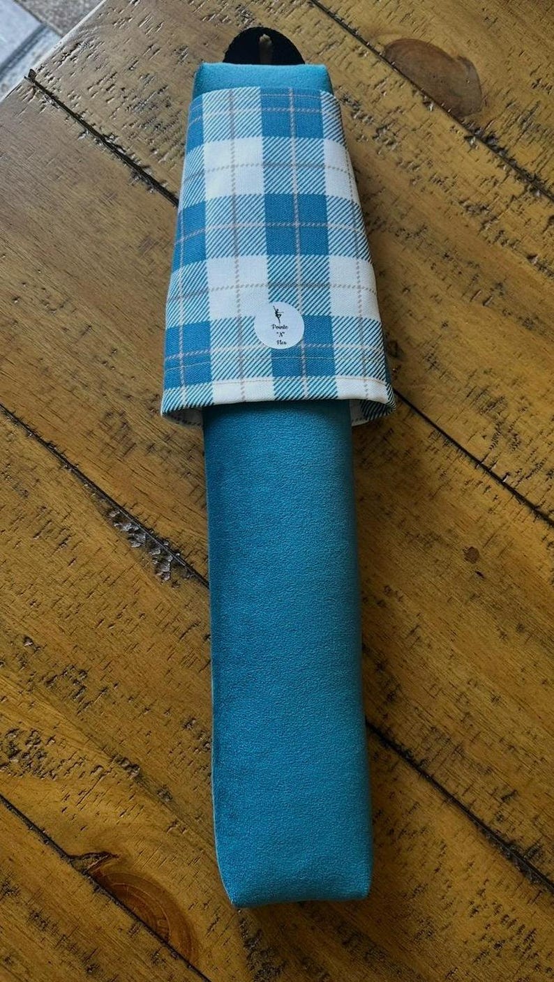 May include: A teal-colored, cylindrical item with a plaid top in white and teal. The item has a loop at the top and a small circular logo. The item is likely a sleeve or cover for a cylindrical object.