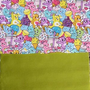 May include: A colorful fabric featuring a pattern of cartoon bears with ice cream, cupcakes, and rainbows. The bears are in various colors, set against a white background. Below is a solid green fabric.