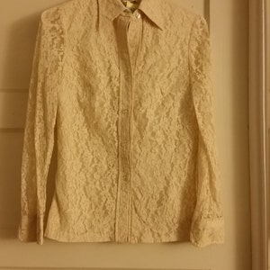 May include: A white lace button-up shirt with long sleeves. The shirt is hanging on a hanger against a white door.