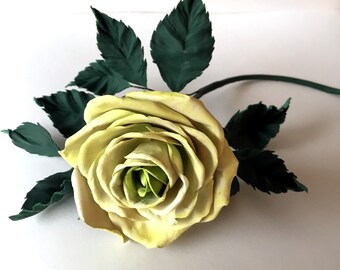May include: A single, pale yellow rose with green leaves. The rose is made of fabric and has a realistic appearance.