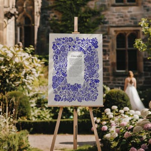 May include: A white canvas with a blue floral design surrounding a Hebrew text document. The canvas is displayed on a wooden easel in a garden setting.