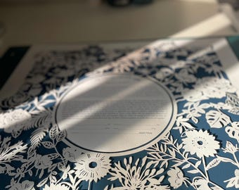 May include: A blue and white paper cut design featuring a circular frame with a floral pattern and two birds. The design is on a white background.