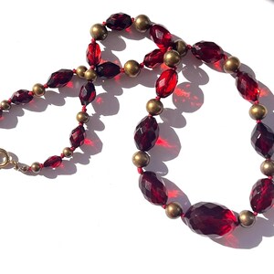 May include: A vintage necklace featuring faceted, deep red beads interspersed with small, round, gold-toned beads. The necklace has a classic design with a gold-colored clasp. The beads are arranged on a red string, creating a striking contrast.