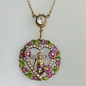 K&ouml;nnte beinhalten: Eine goldfarbene Halskette mit einem herzf&ouml;rmigen Anh&auml;nger, der einen Cherub mit Fl&uuml;geln zeigt, umgeben von rosa Blumen und klaren Strasssteinen.