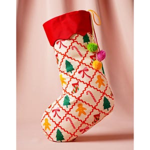 May include: A festive Christmas stocking with a red, scalloped cuff and a cream-coloured body. The body is patterned with red grid lines and festive images of gingerbread men, Christmas trees, and candy canes. It is decorated with colourful pom-poms.