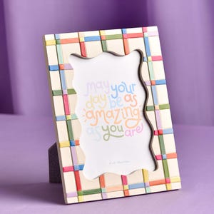 Op de afbeelding: Crèmekleurige fotolijst met een kleurrijk ruitpatroon. De lijst heeft een golvende binnenrand en bevat de tekst "May your day be as amazing as you are." De lijst is 15 x 20 cm.