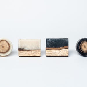 May include: Four decorative cabinet knobs. Two are square, and two are round. The knobs feature wood grain and resin in various colours, including cream, black, and brown. The knobs are designed for furniture and home decor.