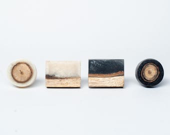 Op de afbeelding: Vier decoratieve kastknoppen. Twee zijn vierkant en twee zijn rond. De knoppen hebben houtnerf en hars in verschillende kleuren, waaronder crème, zwart en bruin. De knoppen zijn ontworpen voor meubels en woondecoratie.