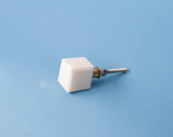 Op de afbeelding: Een witte vierkante meubelknop met een gladde afwerking. De knop is voorzien van een metalen draadeind aan de achterzijde, vergezeld van een kleine metalen ring en een moer voor een veilige bevestiging op meubels of kastdeuren.