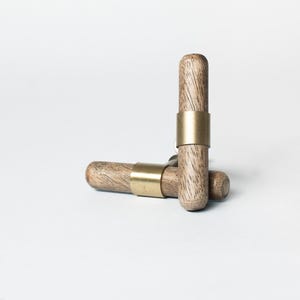 May include: Two wooden cabinet knobs with a natural wood grain finish and a gold-coloured metal band. One knob is upright, and the other is lying horizontally. The knobs are set against a white background.