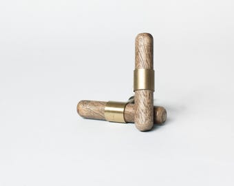 Op de afbeelding: Twee houten kastknoppen met een natuurlijke houtnerf afwerking en een goudkleurige metalen band. Eén knop staat rechtop en de andere ligt horizontaal. De knoppen staan tegen een witte achtergrond.