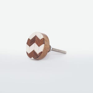 May include: A wooden cabinet knob with a chevron pattern. The knob features a light brown wooden base with a decorative face of alternating dark brown and white chevron shapes. A silver screw extends from the back for installation.