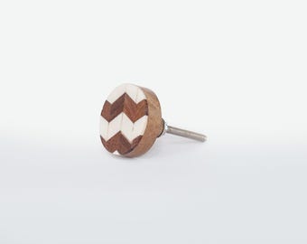 Op de afbeelding: Een houten kastknop met een chevronpatroon. De knop heeft een lichtbruine houten basis met een decoratief oppervlak van afwisselend donkerbruine en witte chevronvormen. Een zilveren schroef steekt uit de achterkant voor installatie.