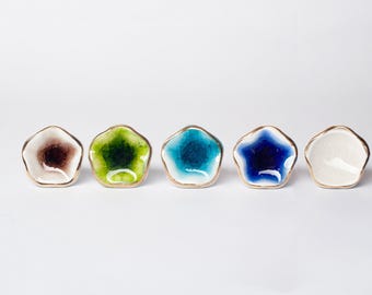 Op de afbeelding: Vijf kleine, stervormige keramische schaaltjes met gouden randen. De schaaltjes hebben verschillende kleuren, waaronder bruin, groen, turquoise, blauw en wit. De schaaltjes zijn in een rij geplaatst tegen een witte achtergrond.