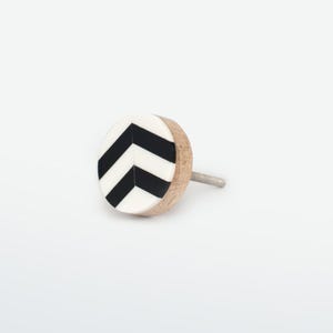 May include: A circular wooden cabinet knob featuring a black and white chevron design. It has a metal stem for attachment. The knob's design is contemporary and minimalist, suitable for various furniture types. The knob's diameter is approximately 4 cm.