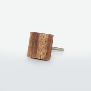 May include: A square wooden cabinet knob with a natural wood grain finish. The knob is attached to a silver-coloured screw. The wood has a warm brown tone, and the design is simple and modern. Suitable for drawers and cabinets.