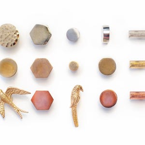 May include: A selection of decorative hardware, including knobs and pulls, in various shapes and finishes. The assortment features round, hexagonal, and cylindrical designs in gold, silver, and copper tones. Two bird-shaped embellishments are also included.