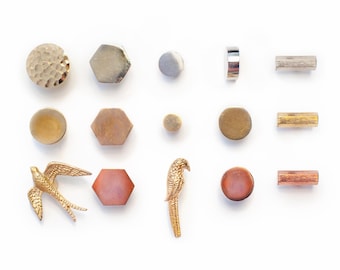 Op de afbeelding: Een verzameling decoratieve hardware, waaronder knoppen en handgrepen, in verschillende vormen en afwerkingen. Het assortiment bevat ronde, zeshoekige en cilindrische ontwerpen in goud-, zilver- en kopertinten. Twee vogelvormige versieringen zijn ook inbegrepen.