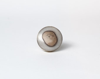 Op de afbeelding: Ronde kastknop met een lichtgrijze hars buitenkant en een natuurlijk houten middenstuk. De houtnerf is zichtbaar in het midden van de knop. Een decoratief hardware-element.