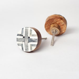 May include: Two wooden cabinet knobs. One knob features a circular design with a cross pattern in shades of grey and white. The other knob is made of wood. Both knobs have a metal screw for installation.