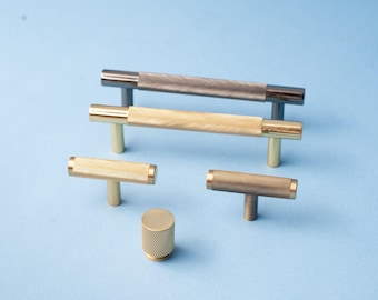 Op de afbeelding: Een collectie van kastknoppen en handgrepen met een gekartelde textuur. De hardware omvat T-bar handgrepen en een cilindrische knop, in goud, brons en gunmetal afwerkingen. Gepresenteerd op een lichtblauwe achtergrond.