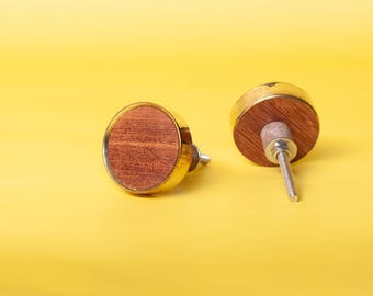Op de afbeelding: Twee decoratieve kastknoppen. Elke knop heeft een ronde, roodbruine houten kern, omlijst door een goudkleurig metalen frame. De knoppen staan tegen een heldergele achtergrond, wat hun ontwerp benadrukt.