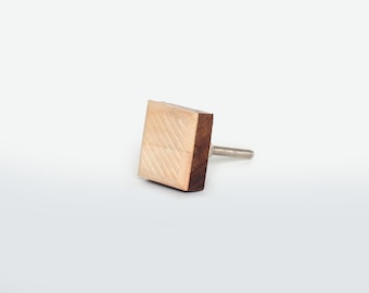 Op de afbeelding: Vierkante houten kastknop met een diagonaal geëtst patroon op de voorkant. De knop is lichtbruin met een donkerdere bruine rand en een zilveren schroef.