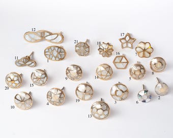 Op de afbeelding: Een verzameling decoratieve kastknoppen en -grepen in verschillende vormen, waaronder ronde, ovale en bloemmotieven. De knoppen hebben een goudkleurige metalen basis met ingelegde parelmoer accenten. De collectie omvat een verscheidenheid aan maten en stijlen.