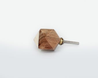 Op de afbeelding: Een geometrische meubelknop met een gefacetteerd ontwerp, bestaande uit een combinatie van natuurlijke bruine houtnerf en een glad wit materiaal. De knop is voorzien van een messingkleurige metalen ring en een zilverkleurige metalen bout.