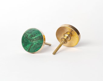 Op de afbeelding: Twee decoratieve kastknoppen. Eén knop heeft een ronde, groene malachietsteen in een goudkleurig metalen frame. De andere is goudkleurig metaal met een schroefdraad. De knoppen staan op een witte achtergrond.
