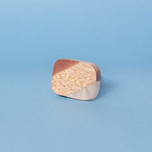 May include: A decorative wooden object with a geometric design. It features sections of light wood, reddish-brown wood, and a white, translucent material. The item is set against a light blue background.