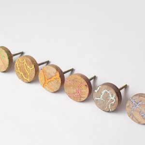 May include: Six wooden cabinet knobs with a circular design. Each knob has a unique pattern of colourful, crackled resin in shades of green, yellow, orange, pink, light blue, and purple. The knobs have a metal stem for easy installation.