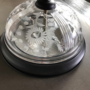 May include: A clear glass dome with a black metal base and etched floral designs. The dome has a knob on top.