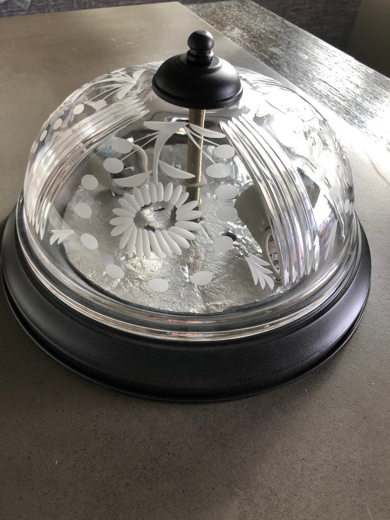 May include: A clear glass dome with a black metal base and etched floral designs. The dome has a knob on top.