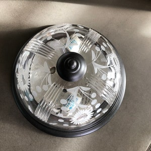 May include: A black ceiling light fixture with a clear glass shade featuring a white floral design. The shade has a textured, ribbed pattern.