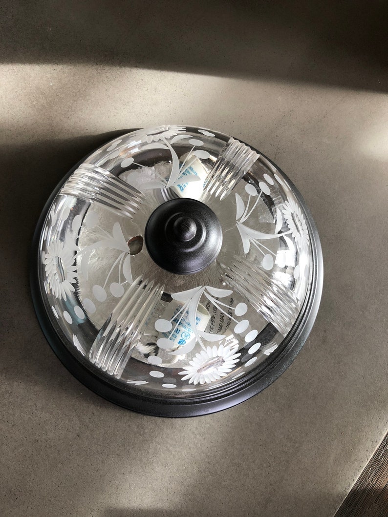 May include: A black ceiling light fixture with a clear glass shade featuring a white floral design. The shade has a textured, ribbed pattern.