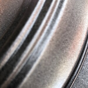 May include: Close-up of a silver metal rim with a black rubber tyre. The metal rim has a smooth, polished finish.