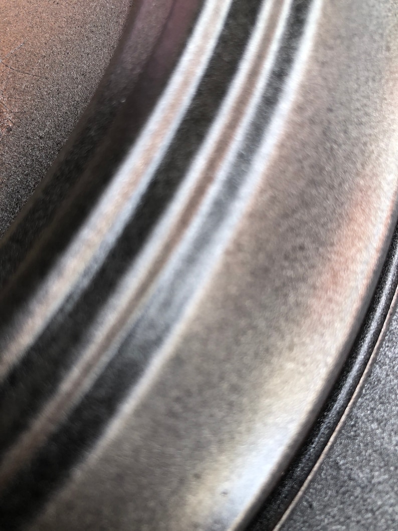 May include: Close-up of a silver metal rim with a black rubber tyre. The metal rim has a smooth, polished finish.