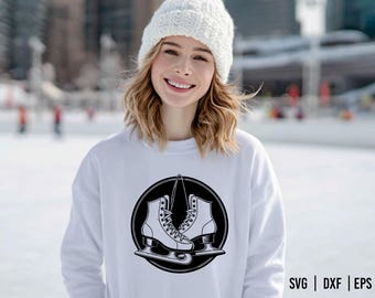 May include: White sweatshirt featuring a black and white graphic of ice skates inside a black circle. The sweatshirt is worn by a person wearing a white knit hat. The background is a snowy outdoor scene.